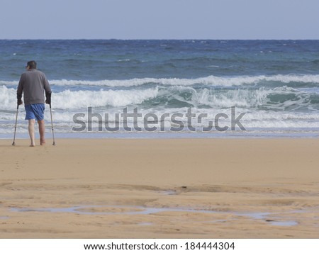 Man with crutches walking on the beach