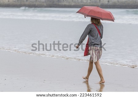 Woman with umbrella walking along the seashore