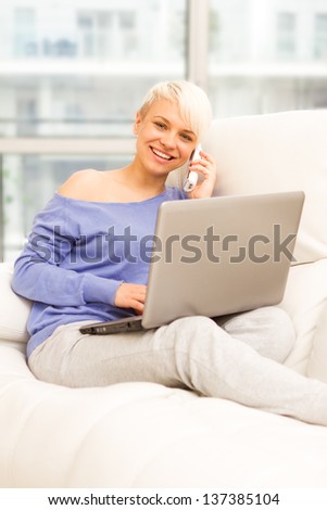 Photo of smiling woman on the sofa with computer and phoning