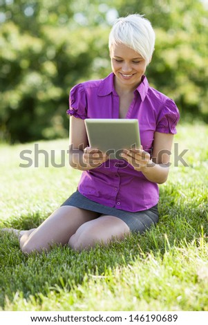 Photo of smiling woman with tablet pc is sitting on the grass while smiling