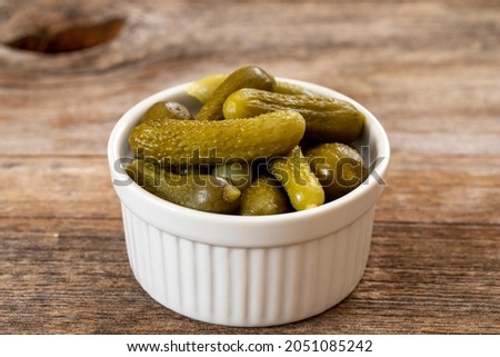 Crunchy pickled cornichons in a white ceramic bowl. Marinated green gherkins. Pickled cucumber. Delicious baby pickles. Tasty canned vegetables Photo stock © 