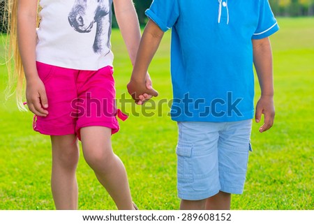 Two children are standing on the glade and holding by hands.