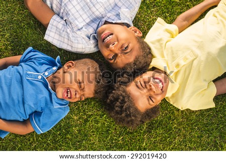 Three dark skin brothers are lying on the sunny glade. They are joking and laughing.