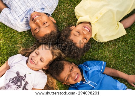 Four beautiful children are laying on the sunny glade with a smile and close eyes.