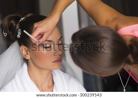 The visagist is correcting makeup. The bride closed her eyes.