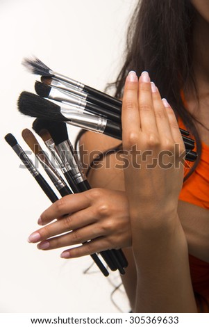 The brunette with long hair is holding makeup brush set. Glamour lady in orange shirt is showing cosmetic brush set closeup.