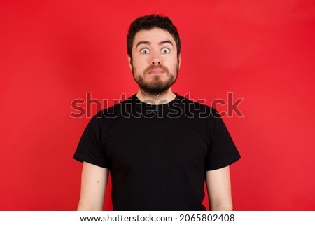 Stunned Young caucasian man wearing black t-shirt over red background stares reacts on shocking news. Astonished MODEL holds breath Foto d'archivio © 
