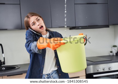Oh my god! Trouble! Upset housewife calling roof repair service while water leaking from ceiling. Woman trying to collecting water at the bucket Foto stock © 