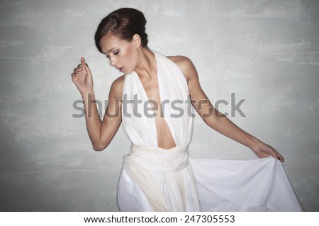 sexy brunette with short hair in an elegant white dress with a deep cut on his chest. with one hand holding the skirt , look down