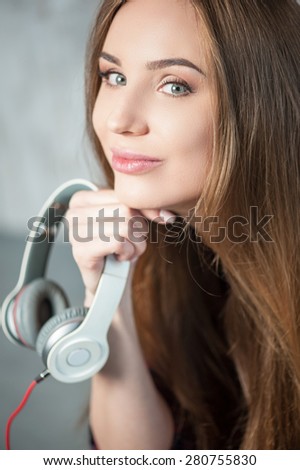 Cheerful hipster woman is holding her headphonesWaist up portrait of beautiful hipster girl with headphones, which she is holding in her hand near her face while smiling and looking at the camera