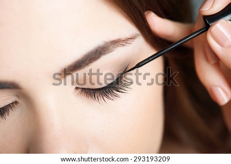 Close-up portrait of beautiful girl touching black eyeliner to her eyelid. Her eyes are closed