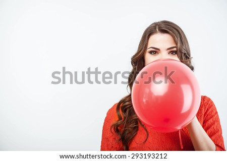 Beautiful woman is blowing red balloon diligently. Her eyes are wide open. Isolated on grey background and there is copy space in the left side