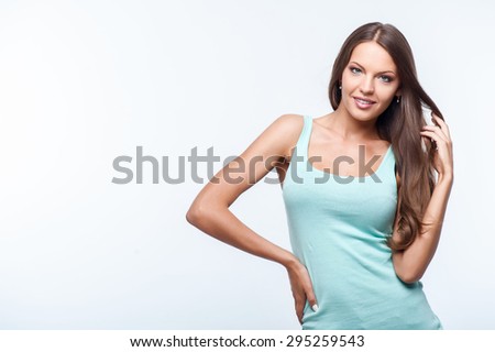 Cheerful woman is posing and smiling. She is touching her hair gently. Isolated on background and there is copy space in left side