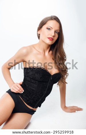 Cheerful girl in seductive black clothing is flirting with someone. She is sitting and looking at the camera with temptation. Isolated on background