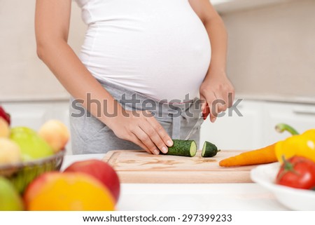 Close up of body of expectant mother cutting fruits and vegetables. She is cooking healthy food. The lady is standing near a table