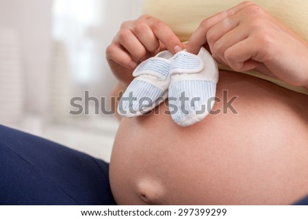 Close up of abdomen of expectant mother. She is touching small baby booties to it