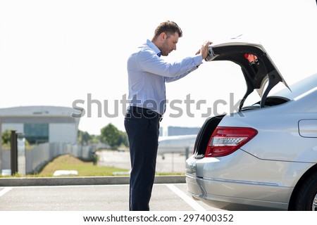 Handsome businessman is preparing for flight in the airport. He is picking up a suitcase from a luggage carrier of his car. He is looking at it seriously. Copy space in left side