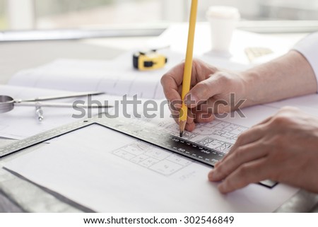 Close up of hands of architect drawing sketches of construction. He is holding a pencil and a ruler