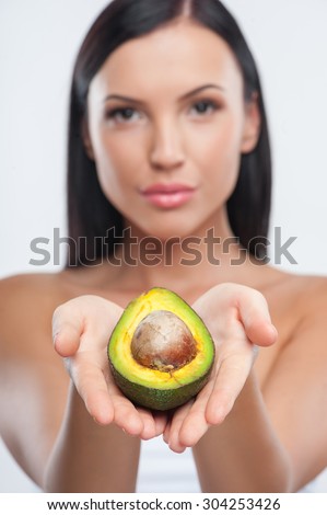Beautiful woman is presenting an avocado. She is holding it in her palms. She is looking at the camera with confidence. Focus on avocado and isolated