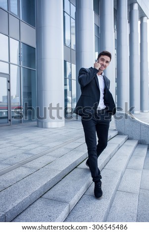 Handsome man in suit is going down steps from his office. He is using a telephone for communication with his business partner. The man is smiling. Copy space in left side