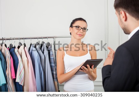 Successful clothes designer is listing to her client attentively. She is looking at him and smiling. The woman is holding a laptop and using it for work