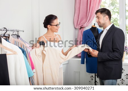 Beautiful clothes designer is showing a fashionable shirt to her customer. The man is touching it and smiling. He likes the work of sewer. The woman is looking at him with joy