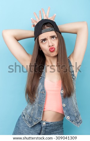 Beautiful styled woman is drawing faces with joy. She is looking up and sending kiss to camera. The woman is standing and putting horns on her head. Isolated on blue background
