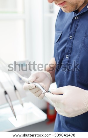 Close up of professional dentist is checking the quality of the medical equipment. He is holding it and touching with concentration