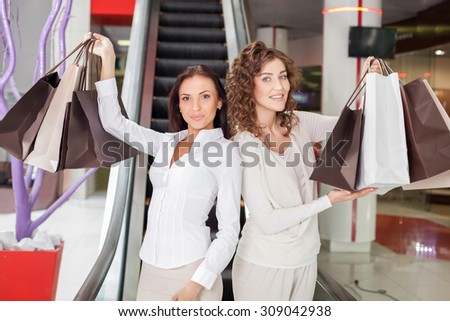 Attractive women are holding many packets of bought clothing and showing it with happiness. They are smiling and looking forward with proud. The friends are standing near excavator in boutique