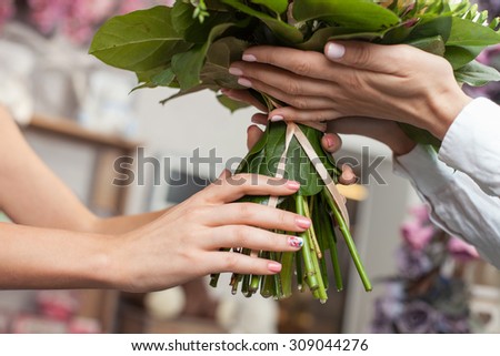 Close up of hands of successful florist giving a bouquet to her customer