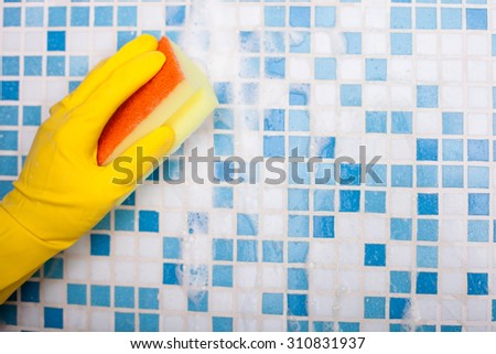 Close up of hand of cleaner in yellow glove. The man is washing a tiled wall with a sponge. There is foam on the tile. Copy space in right side