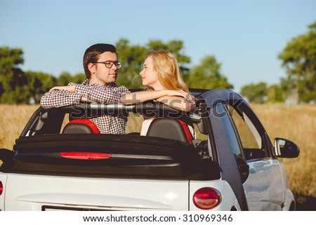 Attractive loving couple is sitting in car and viewing through the open roof. They are looking at each other with love and smiling. They are enjoying the nature together