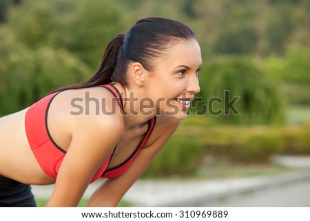 Attractive female athlete is kneeing at start position. She is smiling and looking forward with concentration. The woman is smiling. Copy space in right side