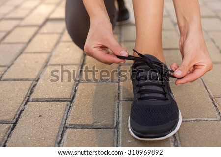 Close up of legs of sport girl lacing her sneakers. The woman is kneeing on the footpath in park