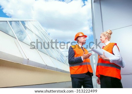 Handsome architect and his colleague are talking about new project. They are standing outdoors and smiling. The workers are looking at each other with inspirations. The woman is holding a blueprint