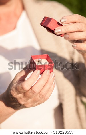 Close up of hands of mature woman holding a little box of gift. She is standing and openting a box. There is a gold ring in it