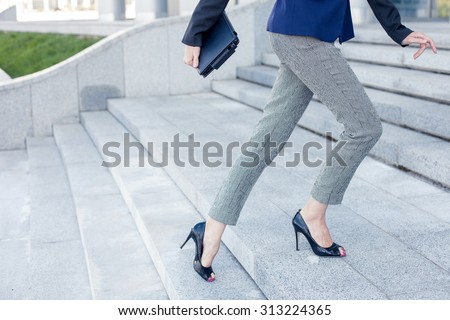 Close up of legs of businesswoman moving upstairs to her office. She is holding a tablet in her hand. Copy space in left side