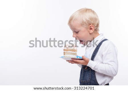 Cheerful boy is eating a cake with enjoyment. He is holding a plate and opening his mouth widely. The boy is looking at the piece of cake with appetite. Isolated and copy space in left side