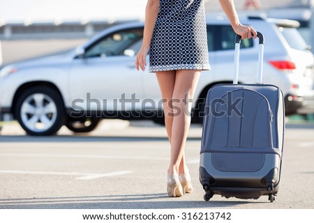 Close up of legs of pretty woman going to her car with luggage. She is wearing dress and shoes on high heels. Copy space in left side