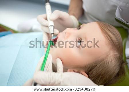 Close up of hands on dentist drilling human teeth carefully. The boy is sitting in medical chair and opening mouth. He is looking at man with trust