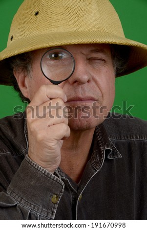 Mature man in pith helmet with a magnifying glass/Mature Explorer/Man is looking through magnifying glass