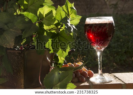 Wine sparkles in the late afternoon sun/Sparkling Red Wine?Grapes and leaves surround a glass of sparkling red wine in a glass.