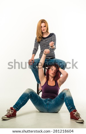 Two angry women connected by a pair of handcuffs wearing jeans, blond and red-haired, barefoot and red chucks, sitting over white background