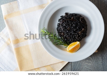 Black risotto with seafood on white plate with lemon and rosemary