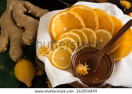 Sliced lemon and orange in basket with honey, ginger root and lemon behind