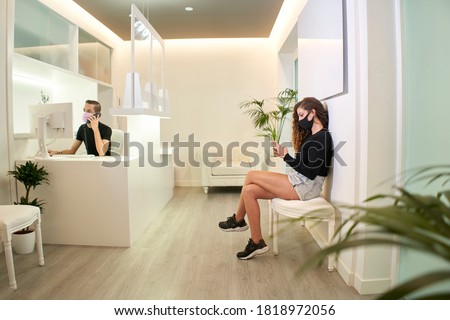 Patient waiting at the reception of the dental, gynecological or aesthetic clinic. The patient is using her smartphone while the receptionist takes a call. Medical concept. Foto stock © 