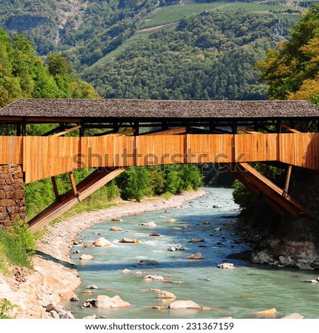Wooden Bridge over the Adige River at the Foot of the Italian Alps