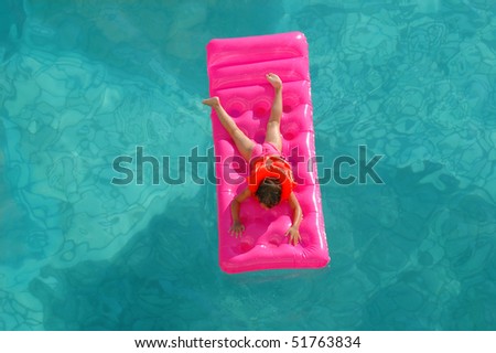 The little girl floats on an inflatable mattress in pool