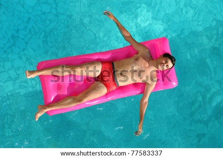 Young man floating on a mattress in water pool