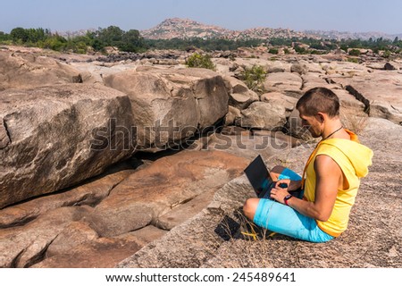Young man sitting on the mountain with beautiful view and working on the laptop.